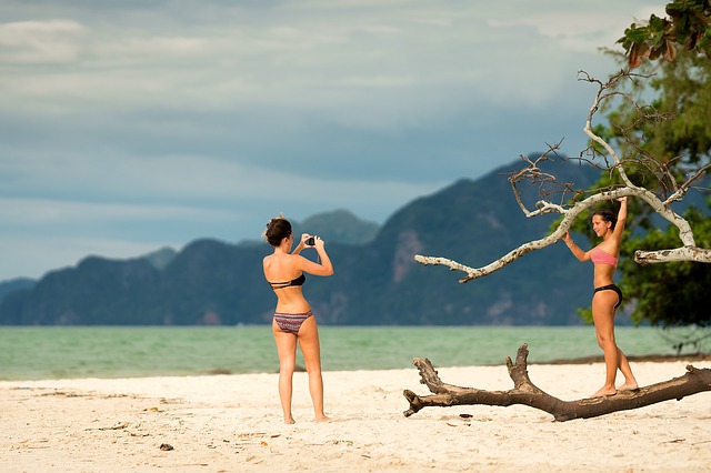 Two women in bikinis on a beach taking photos.